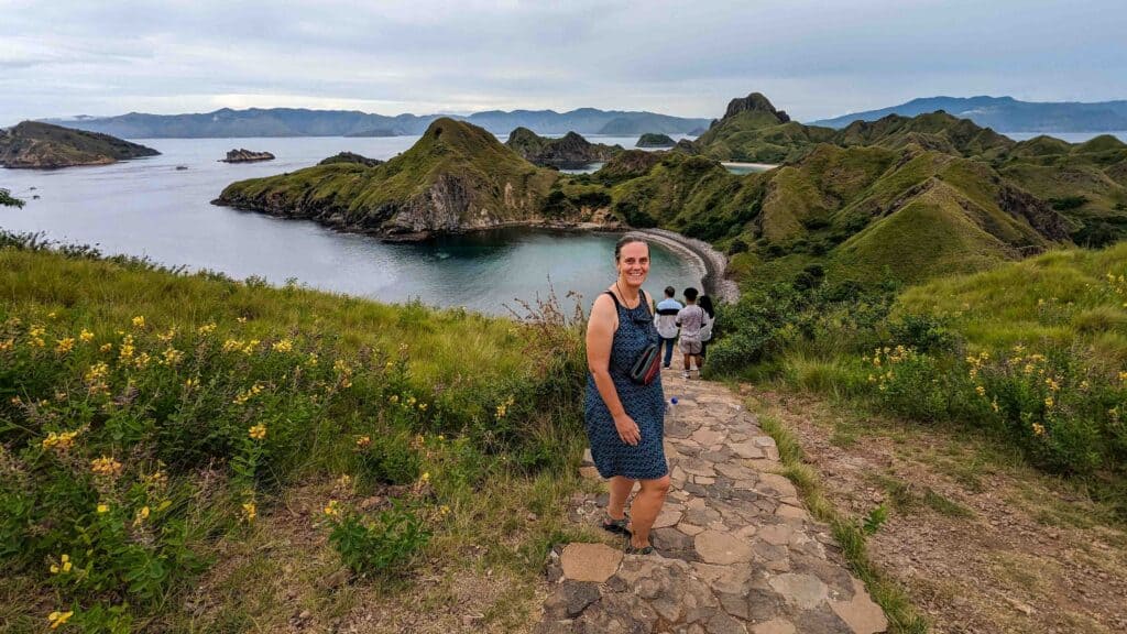 A woman standing on the top of a mountain with ocean behind her