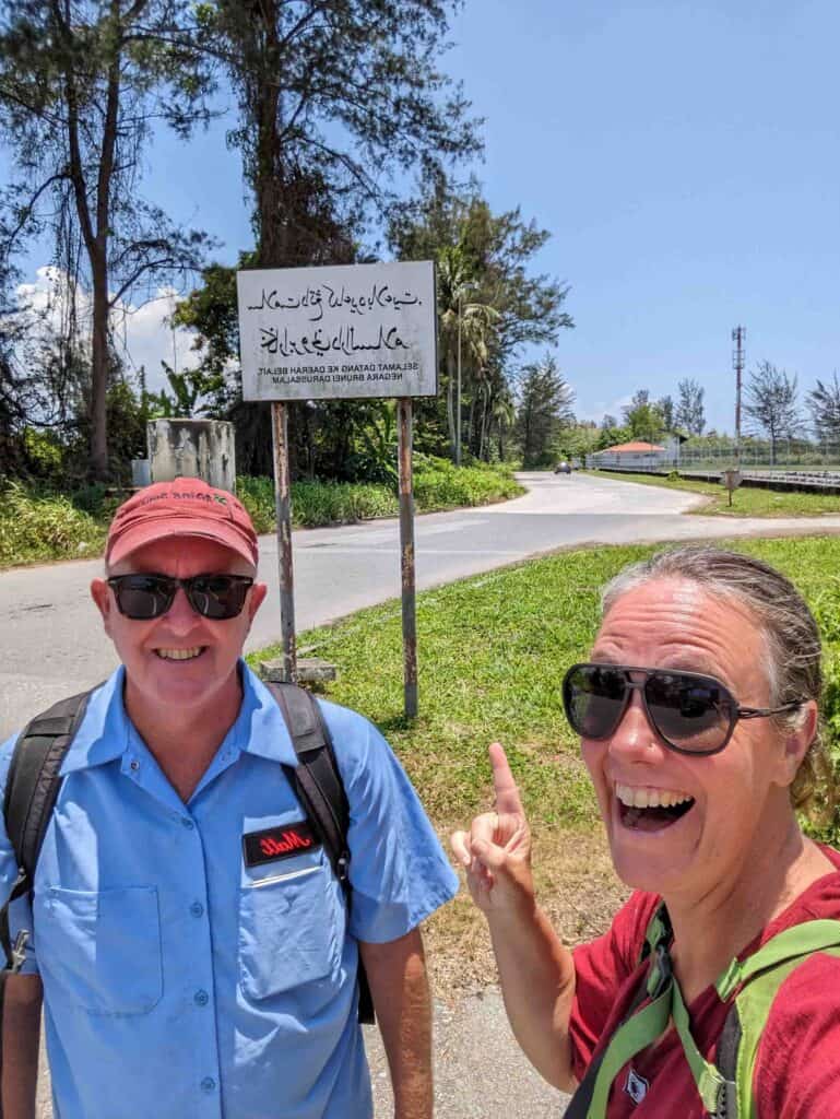 2 people in front of the Welcome to Bruneii Sign