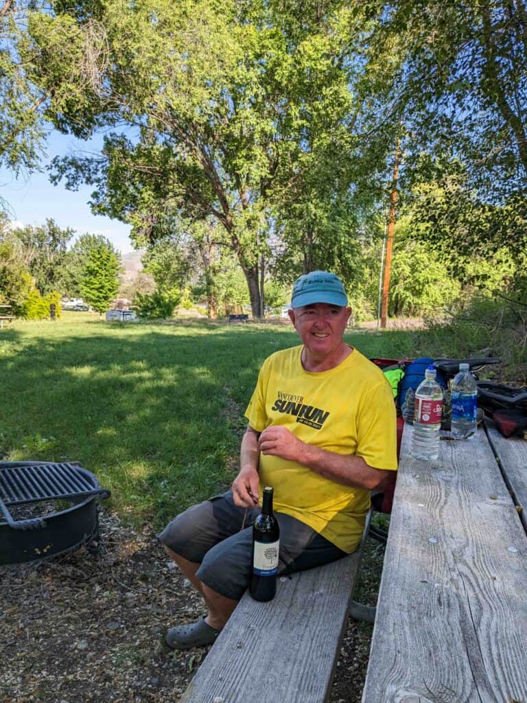 Man sitting on a picnic table with a bottle of wine